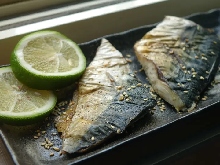 To grillede makrelfileter med sprødt skind, limeskiver og sesamfrø på et mørkt fad